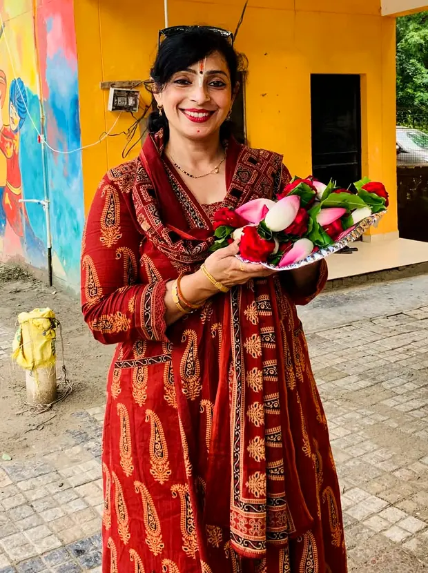 Dr. Reena Soni in a red Ajrakh suit holding a plate of flowers